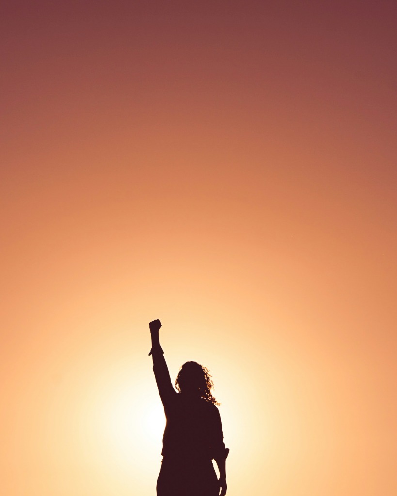 Silhouette of a woman raising her fist against a golden sunset